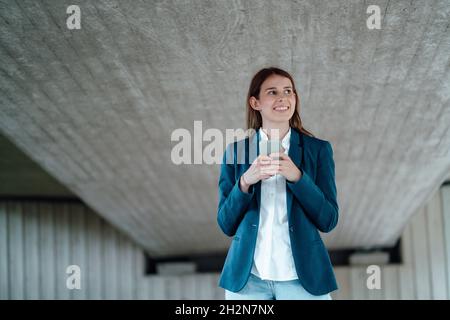 Smiling female freelancer surfing net through smart phone in basement Stock Photo