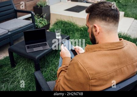 Male freelancer text messaging through smart phone while sitting at backyard Stock Photo