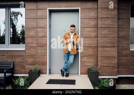 Man using mobile phone while leaning at doorway Stock Photo