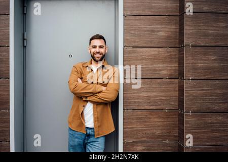 Smiling handsome man standing with arms crossed while leaning at doorway Stock Photo