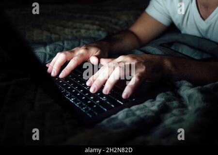 Mid adult man typing on laptop in dark room Stock Photo