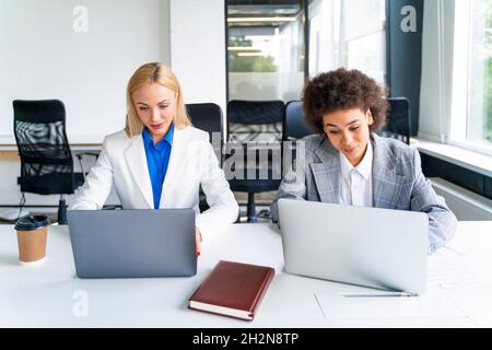 Female coworkers using laptops while working in office Stock Photo