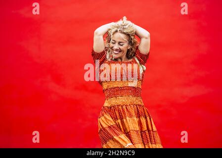 Mature woman with hands in hair standing against red background Stock Photo