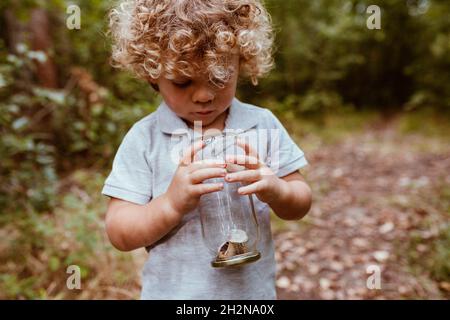 Cute boy holding glass jar with snails in forest Stock Photo