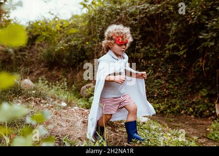 Boy wearing cape walking in forest Stock Photo