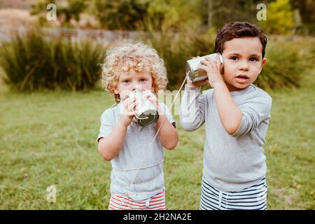 Cute boys communicating with tin can phone on meadow Stock Photo