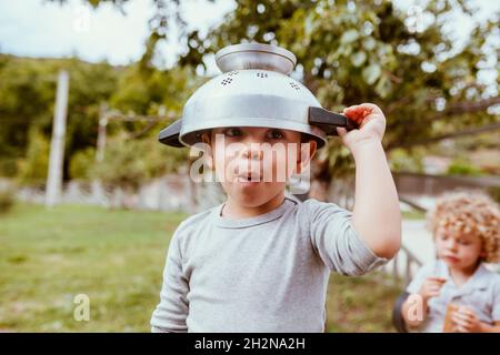 Baby boy playing on kitchen counter with strainer over his head Stock Photo