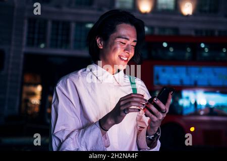 Smiling handsome man surfing net through mobile phone in city at night Stock Photo
