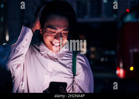 Happy young man with hand in hair using smart phone at night Stock Photo