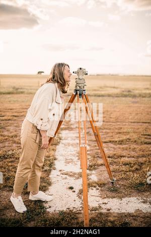 Mature woman looking through theodolite at field Stock Photo