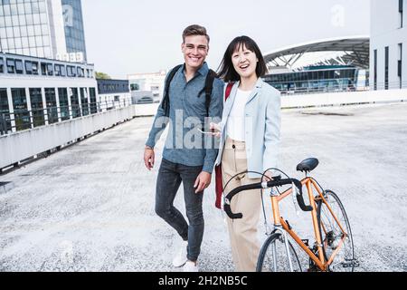 Happy male and female friends with bicycle walking on parking garage rooftop Stock Photo
