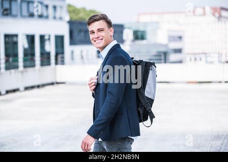 Smiling businessman with backpack walking on rooftop Stock Photo