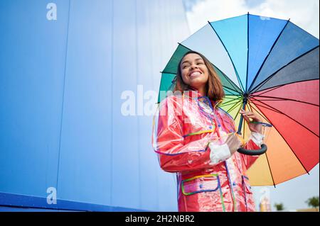 Young woman with multi colored umbrella in front of blue wall Stock Photo