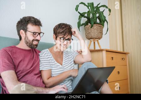 Smiling mid adult couple using laptop while sitting on bed Stock Photo