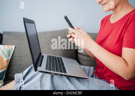 Female freelancer with laptop using smart phone on sofa at home office Stock Photo