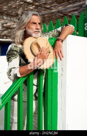 Bearded man with sun hat leaning on railing Stock Photo