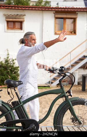 Smiling man with bicycle waving hand Stock Photo