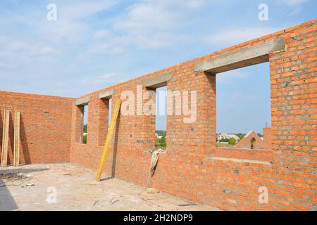 Unfinished Red Brick House Wall  under Construction without Roofing.  Attic Windows Concrete Lintel Frame Construction. House construction site. Brick Stock Photo