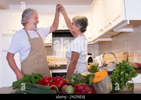 Senior couple holding hands while dancing in kitchen Stock Photo