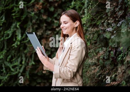 Smiling young female professional using digital tablet while standing by plants Stock Photo