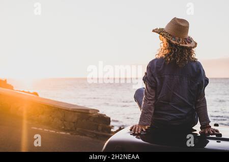 Woman looking at sea while sitting on car during sunset Stock Photo