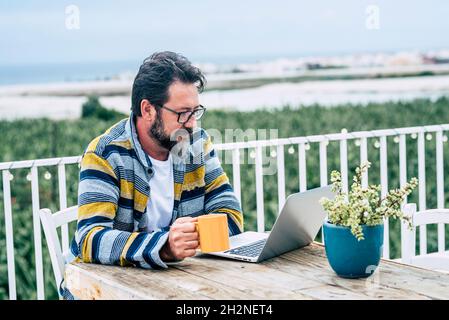 Bearded man with coffee mug using laptop while working on rooftop Stock Photo