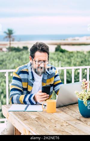 Bearded man with laptop using mobile phone at table Stock Photo