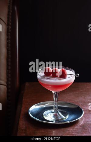 Clover Club Cocktail with Raspberries and Egg White Foam in Coupe Glass in Dark Luxurious Bar Stock Photo