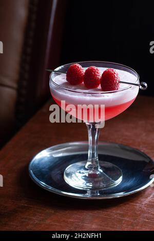 Clover Club Cocktail with Raspberries and Egg White Foam in Coupe Glass in Dark Luxurious Bar Stock Photo