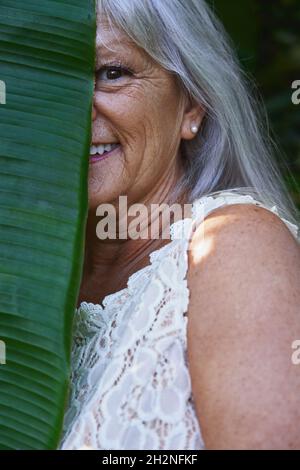 Half face of smiling senior woman covered with leaf Stock Photo