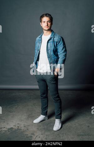 Young man wearing denim jacket while standing with hands in pockets Stock Photo