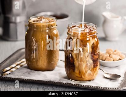 Milk or Cream Being Poured Into Mason Jar Full of Iced Coffee or Iced Latte with Straws Stock Photo