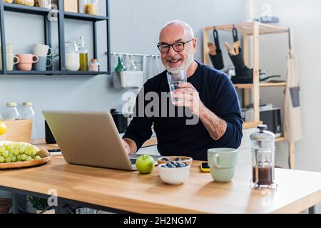 Senior man drinking water while using laptop at home Stock Photo