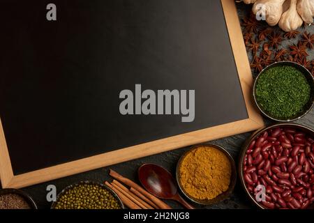 spices concept diverse tones and kinds of spices placed into spoons and small bowls arranged on the black background with the wooden black board. Stock Photo