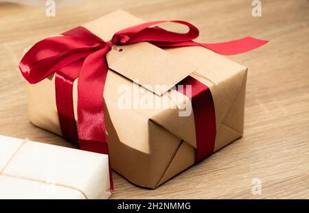 Christmas brown gift boxes and red ribbon with tag paper lay on the table, front view with copy space. Stock Photo