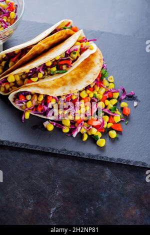 Vegetarian tacos with various vegetables, guacamole and sliced lime on dark background. Tacos with sweet corn, purple cabbage and pepper on a slate bo Stock Photo