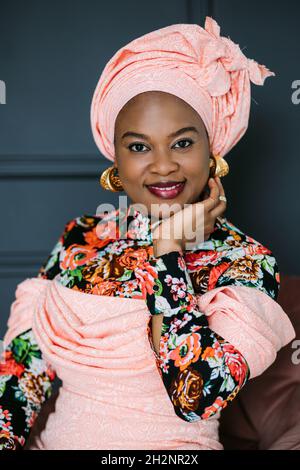 Studio close up portrait of African woman with bright makeup and stylish jewerly, wearing pink colorful dress and ethnic headwrap, posing in studio. Fashion style.