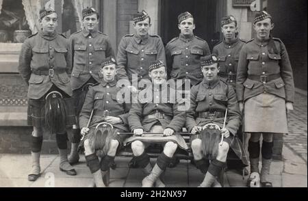 A First World War era group picture of nine kilted soldiers from the Liverpool Scottish, the 10th battalion of the  King's (Liverpool) Regiment. One of the four men standing in the back row is described as having seen service in German East Africa (although the battalion itself did not). Two of thestanding men are described as drafts due to leave for "the front" in the next week. Others in the group are described as rookies. One of the soliders is named Frank. There is a sign saying "Casteford" suggesting the picture was taken in Yorkshire. A woman looks out from the window. Dated 22/04/1916. Stock Photo