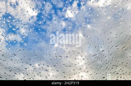 Raindrops on glass window with blue sky and white cloud background Stock Photo