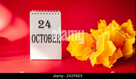 October 24, the date is written on a white notebook framed by foliage on a red background. Stock Photo