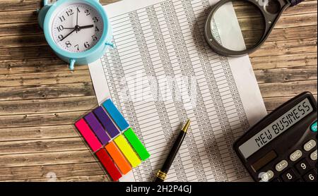 New calculator case. Next to him is a document with numbers, a pen, a magnifying glass and an alarm clock on a wooden background. Stock Photo