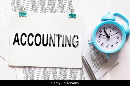 Accounting, the word is written on a notebook that lies on papers with numbers, a pen and an alarm clock Stock Photo