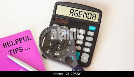 Agenda, the text is written on a calculator, near a colored notebook with useful tips, a magnifier and a pen on a white background Stock Photo