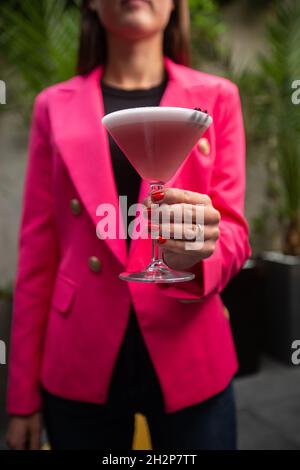 Girl with Pink Clover Club Cocktail in Martini Glass with Layer of Foam and flower Garnish. Stock Photo