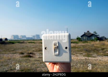 Hand holding discarded plastic flat plate light switch and the Dungeness Nuclear Power Station landscape in Kent England UK Great Britain KATHY DEWITT Stock Photo