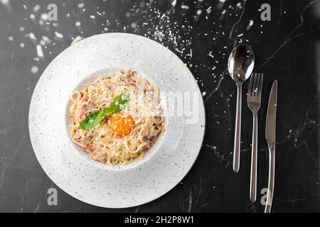 Pasta Carbonara. Spaghetti with bacon, parmesan, cream sauce and egg yolk on black marble background. Mediterranean gourmet food. Stock Photo