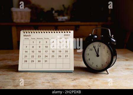 March 2022 calendar and black vintage clock on wooden table Stock Photo