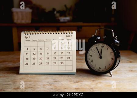 April 2022 calendar and black vintage clock on wooden table Stock Photo