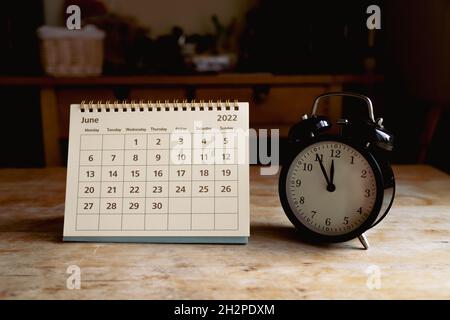 June 2022 calendar and black vintage clock on wooden table Stock Photo