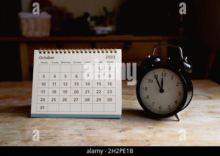 October 2022 calendar and black vintage clock on wooden table Stock Photo